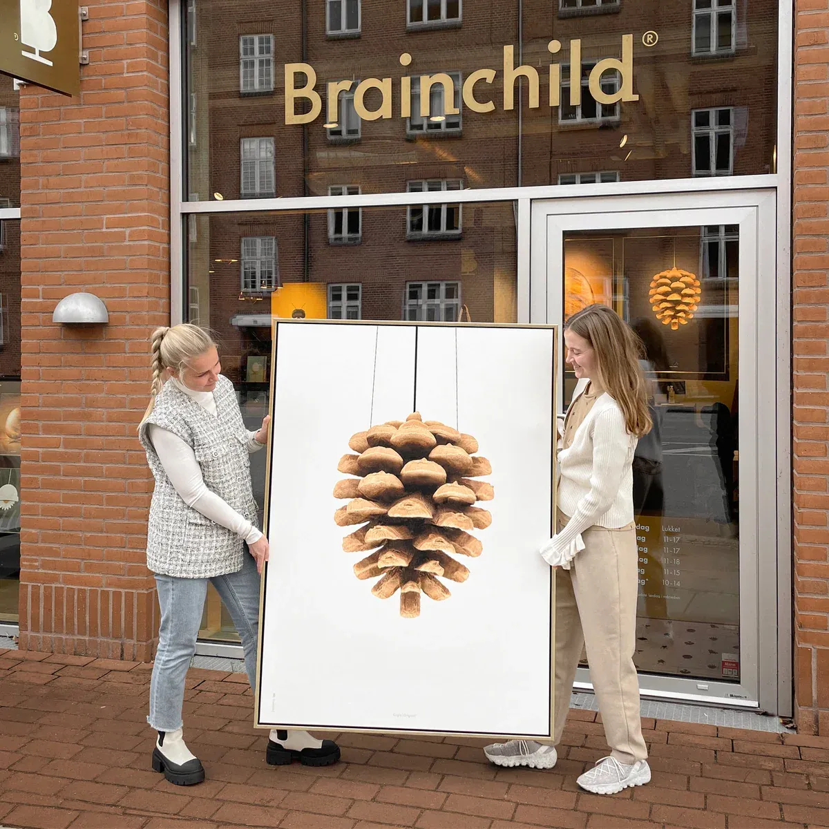 To medarbejdere holder en stor kogleplakat foran butikken