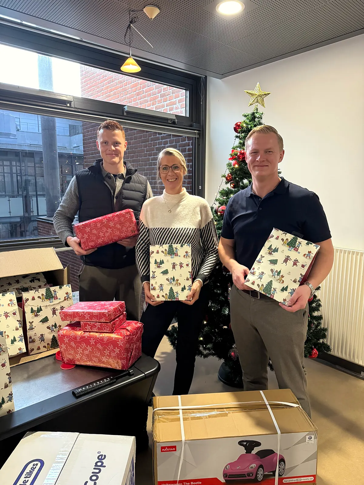 Tre fra NORDIC AD PARTNER med indpakkede julegaver foran et juletræ på børneafdelingen i Esbjerg